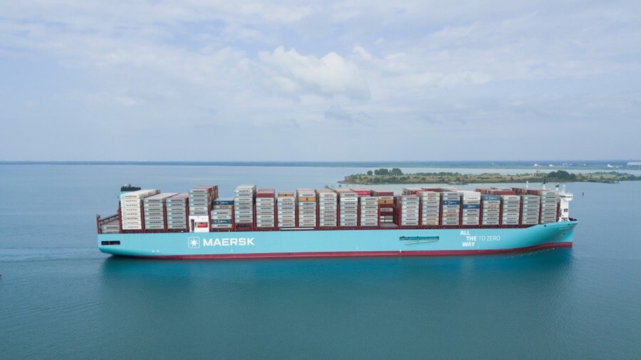 A large container ship navigates through the open ocean under a clear blue sky.