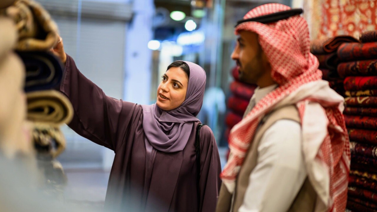 A man and woman examine colorful fabric rolls in a store, discussing their options for a sewing project.
