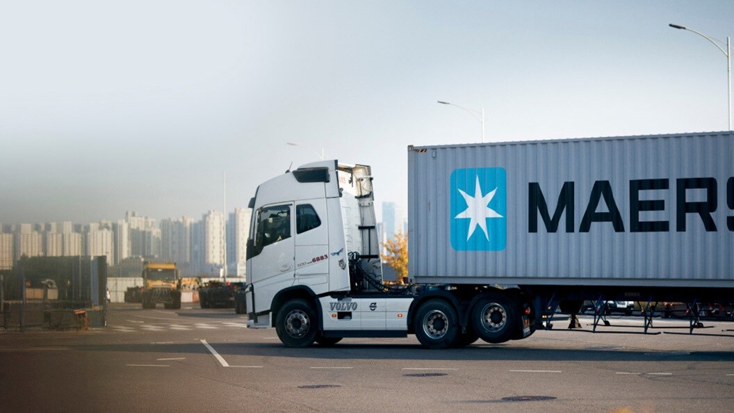 Um caminhão grande exibindo a palavra "Maersk" proeminente na lateral, estacionado em uma rua da cidade.