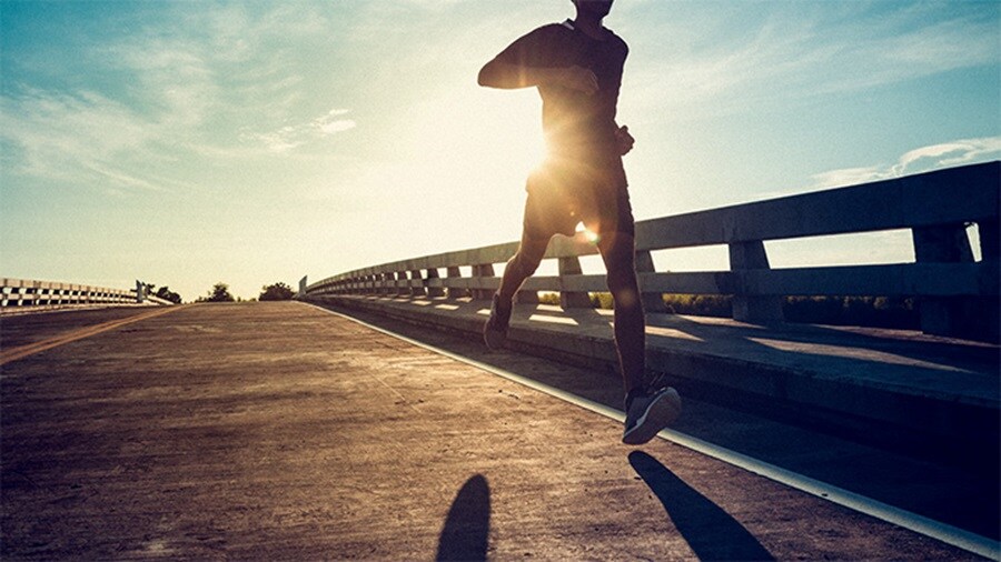 Runner silhouetted against sunrise on a bridge.