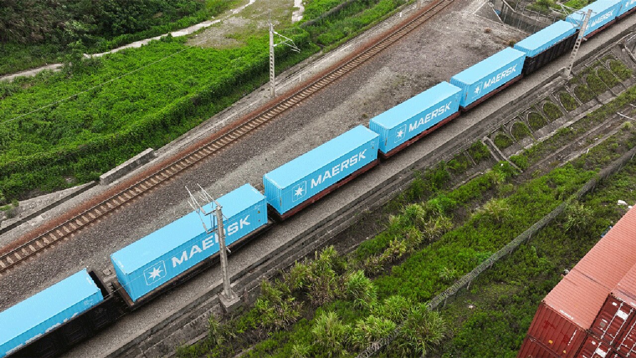 Aerial view of a blue train traveling along a railway track surrounded by greenery.