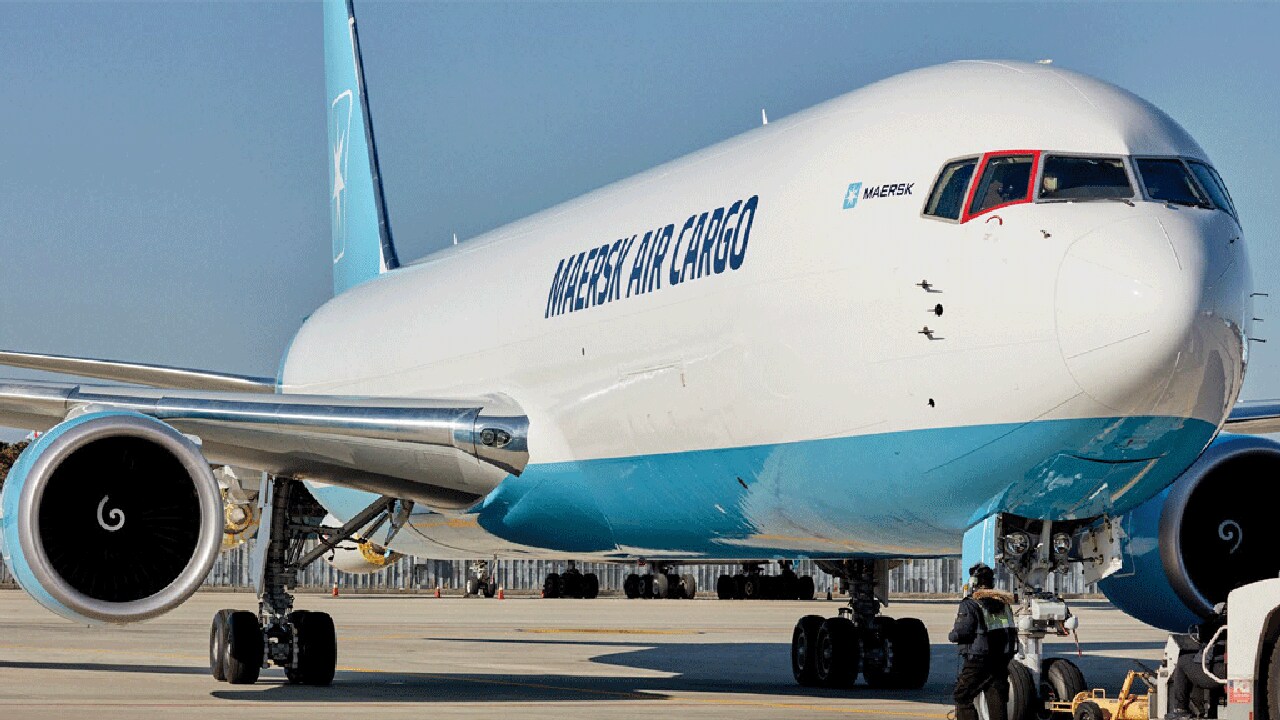 A Maersk Air Cargo plane is parked on the tarmac as a ground crew member works near the nose wheel.