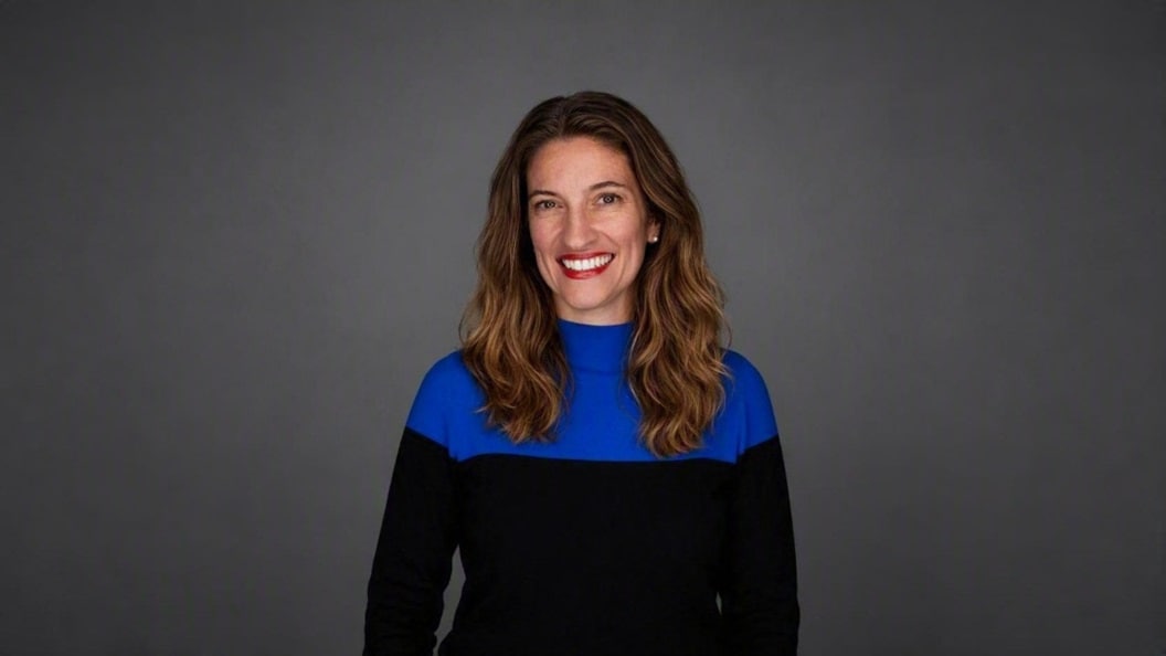 Portrait of a person in a blue and black top against a grey background.