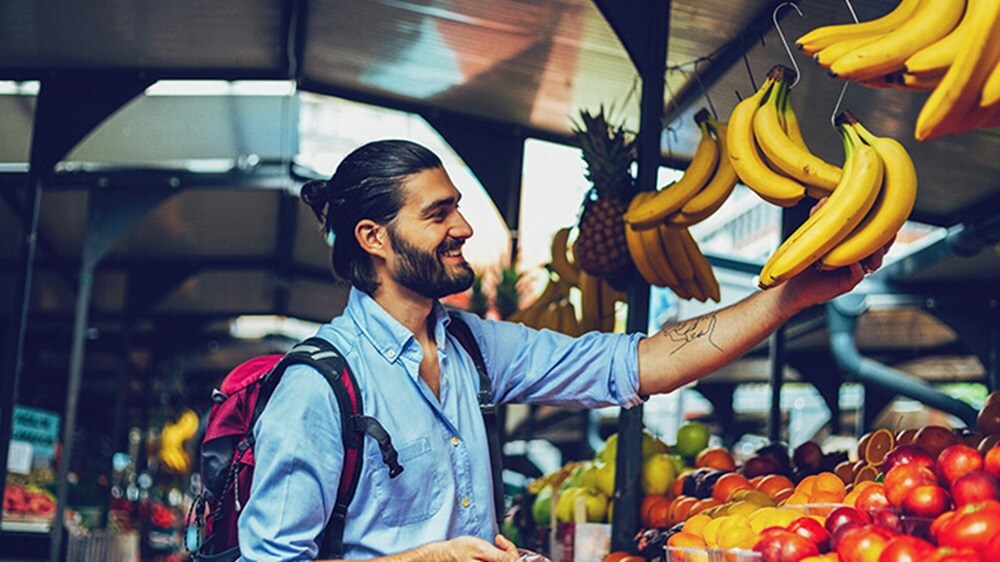 A smiling man looking at bananas in a fruit market. 