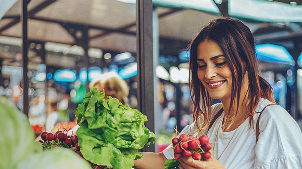 Perishables logistics – A smiling woman buying perishables like fruits and vegetables in a market.