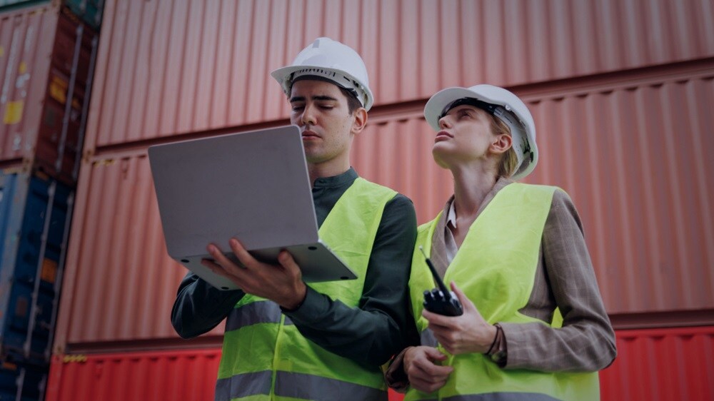 Two professionals reviewing logistics information near cargo containers