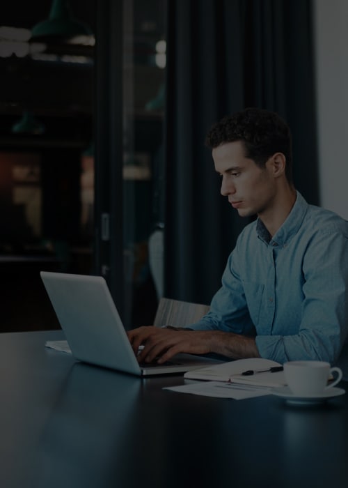 A man engaged with his laptop at a table, surrounded by a relaxed and informal setting.