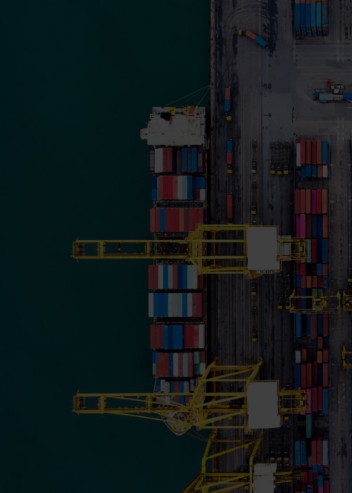Aerial top view of a busy container port with cranes loading shipping containers and organized stacks along the terminal