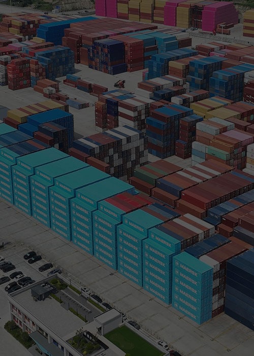 Aerial view of a large intermodal container yard with stacked shipping containers in various colors and brands.