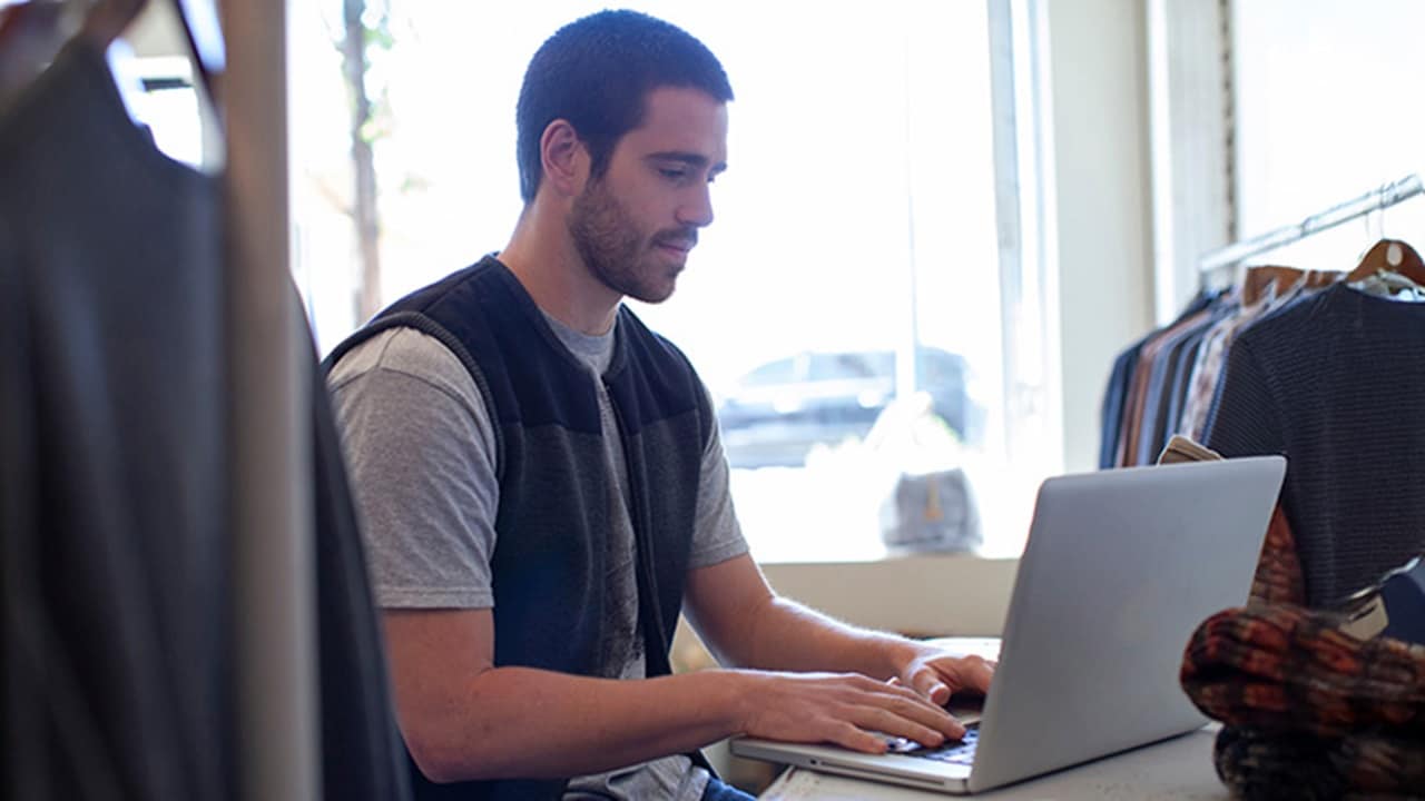 Man working on a laptop in a clothing store.