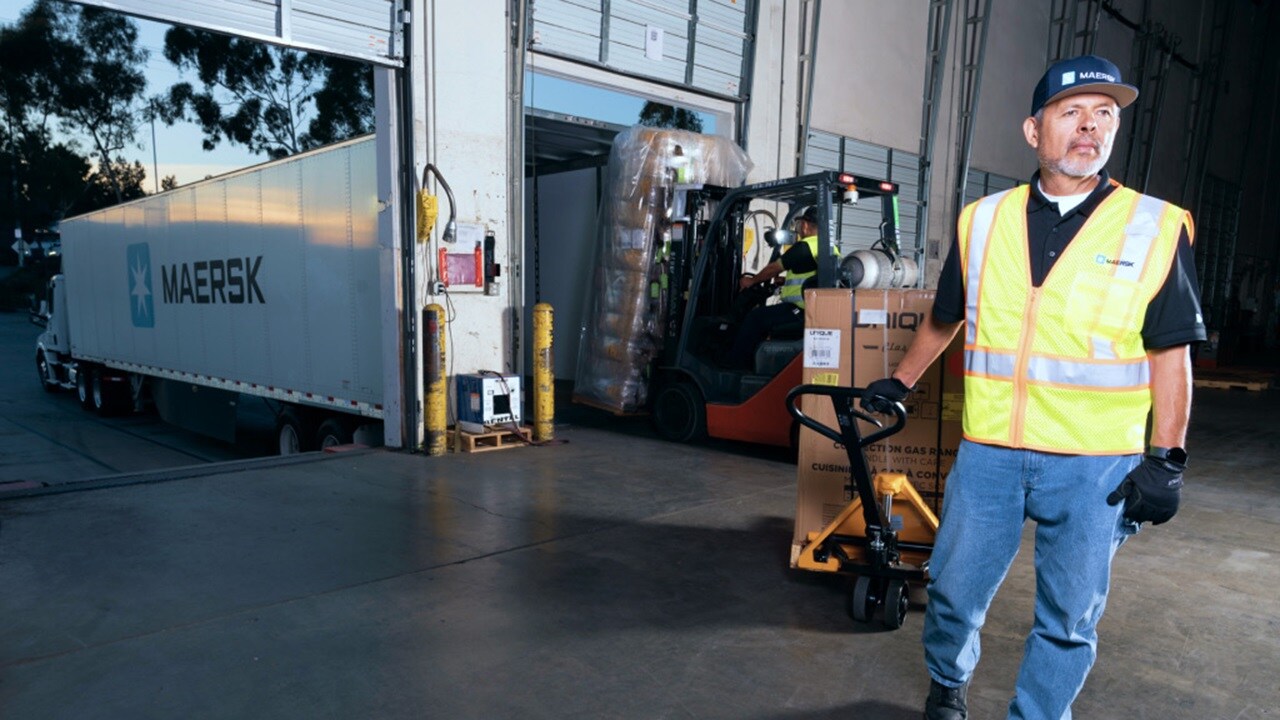 Складские работники за рулем вилочного погрузчика загружают упакованный груз на деревянном поддоне в контейнерный автомобиль Maersk.