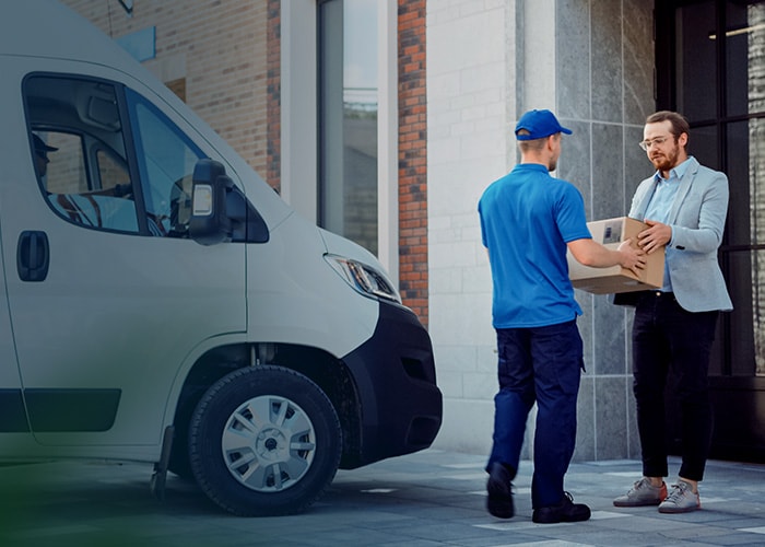 E-commerce last-mile delivery – A delivery man handing a package to a customer with a truck containing packages behind him.